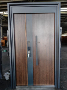 Modern Security Door featuring a dark metal frame, a wood-grain finish panel, and a long vrtical handle with an integrated electronic lock